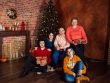 A family posing with Christmas gifts by a decorated tree indoors, exuding holiday warmth.