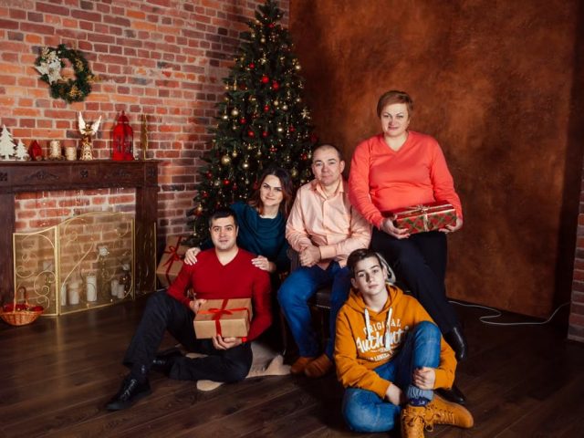 A family posing with Christmas gifts by a decorated tree indoors, exuding holiday warmth.